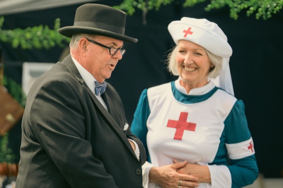A smiling costumed man in a bowler hat beside a woman in a nurse-style costume.