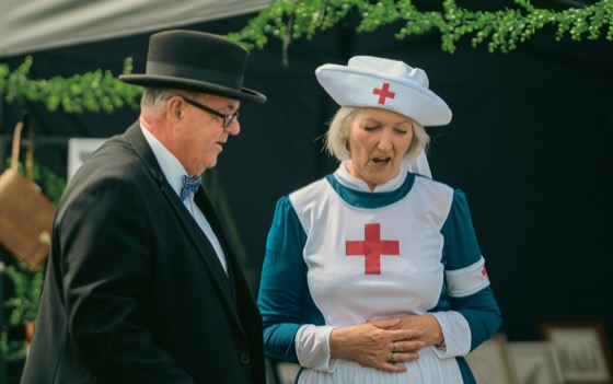 A costumed man in a bowler hat and a woman in a nurse-style costume looking down during a quiet moment.