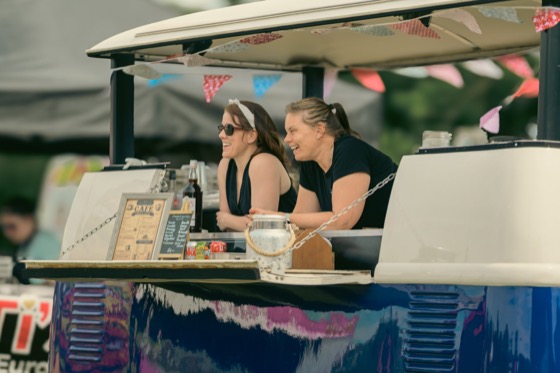 Two smiling women at a cafe van decorated with bunting during a 1940s themed event.