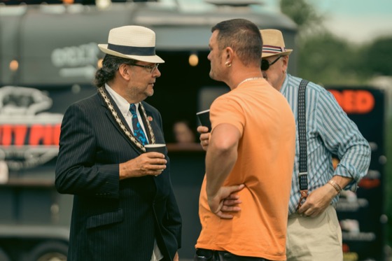 Three men in conversation at a 1940s themed event, including one in a pinstripe suit and straw hat.