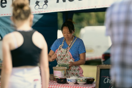 A woman in a blue dress and apron preparing food at an outdoor event stall.