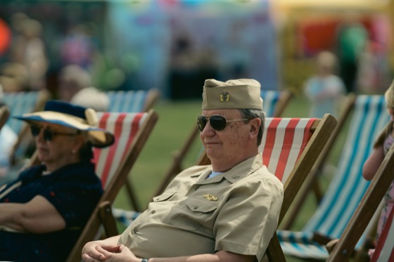 A man in khaki military-style uniform sitting in a deckchair at a public event.