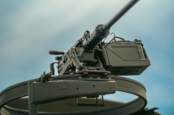 Mounted gun detail on a military-style vehicle against a blue sky.