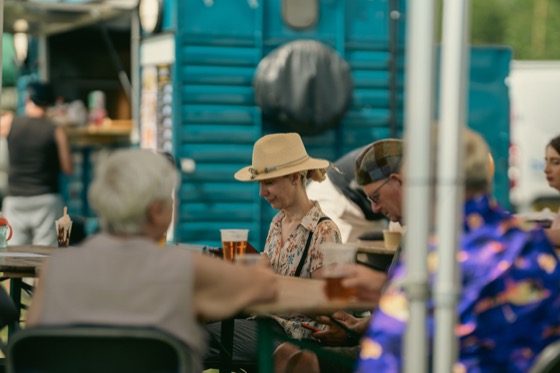 People sitting at outdoor tables with drinks during a busy public event.
