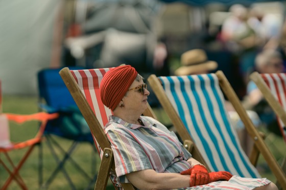 A woman in a red turban and striped dress sitting in a deckchair at a 1940s themed event.