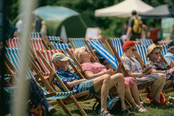 Four adults relaxing in striped deckchairs at a sunny 1940s themed event.