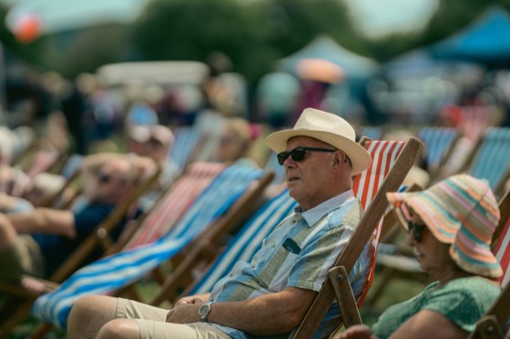A man in a straw hat and sunglasses sitting among striped deckchairs.