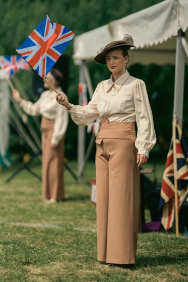A woman in period-style clothing holding a Union Jack flag at a 1940s themed event.