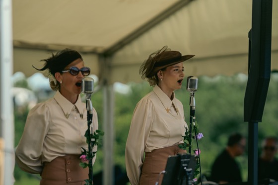 Two women performing with vintage-style microphones at a 1940s themed event.