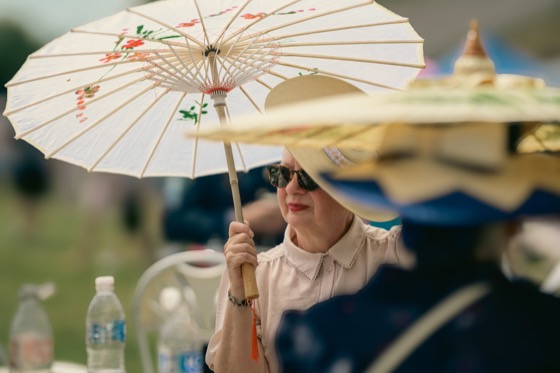 Close view of a woman under a white parasol at a 1940s themed event.