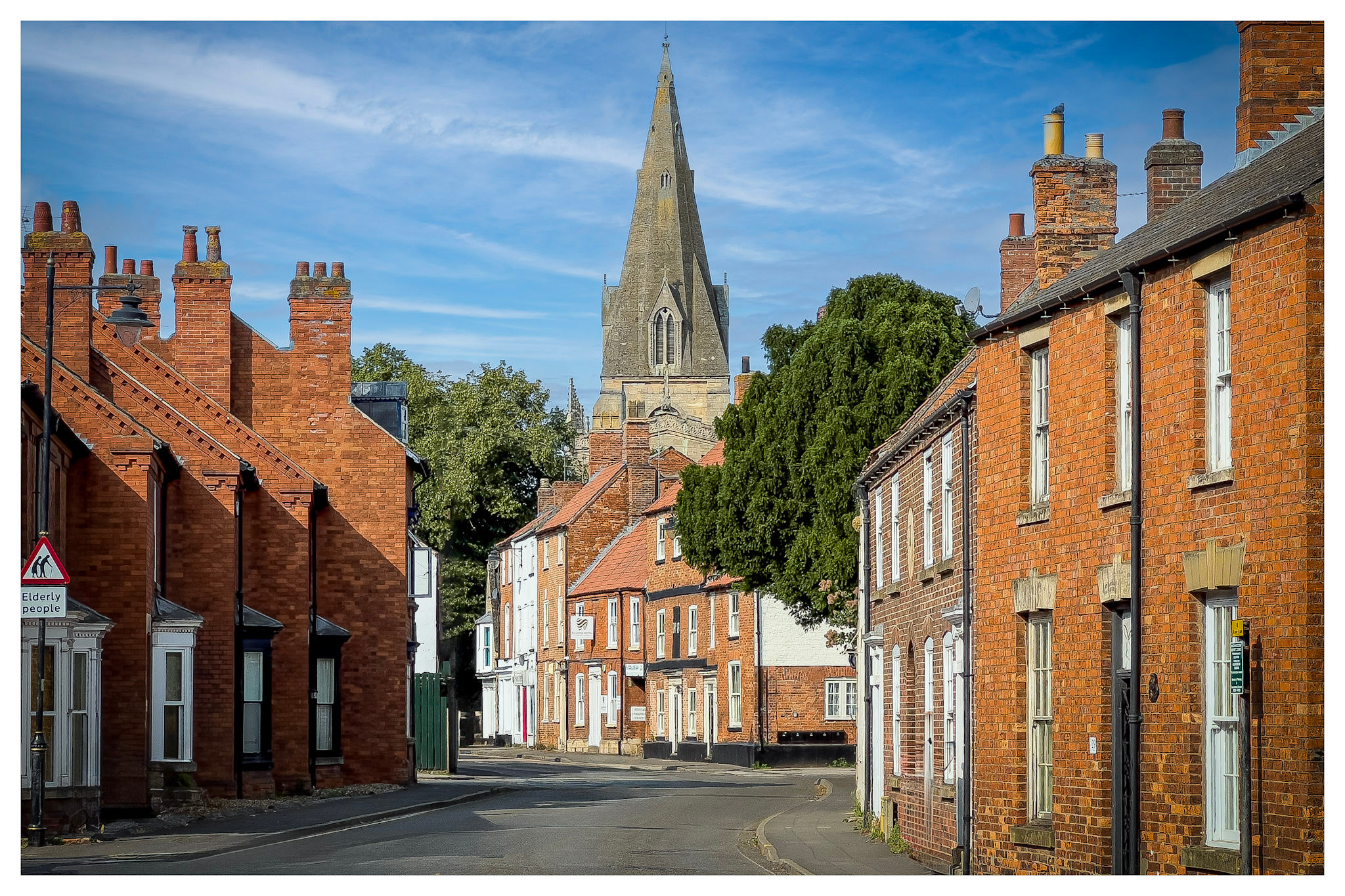 Eastgate's red-brick terraces lead towards the stone spire of St Denys' Church in Sleaford under a blue sky.
