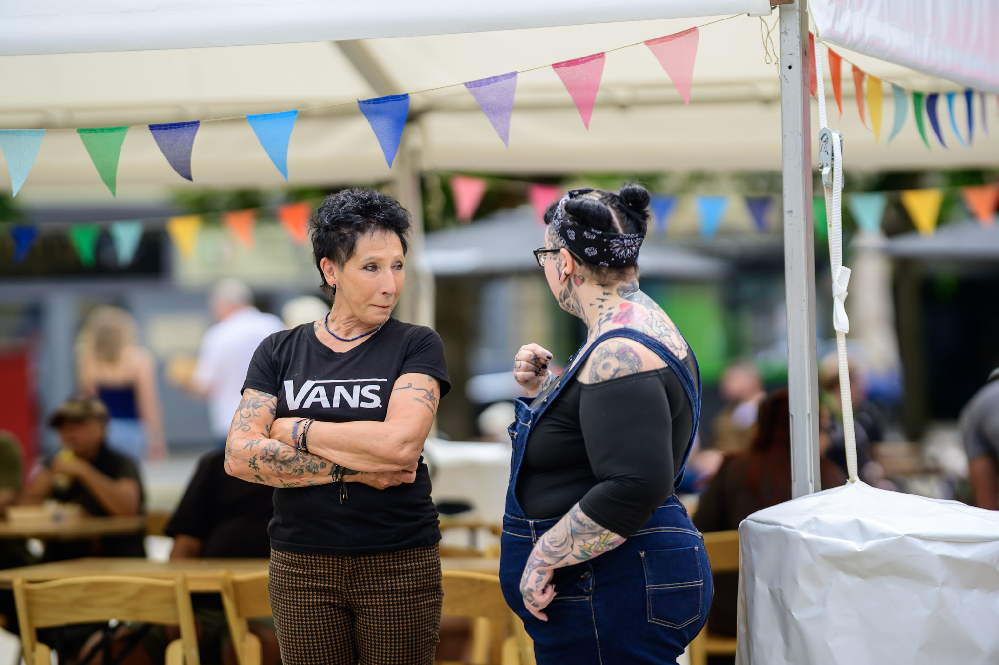 Two tattooed women talking under bunting at the festival